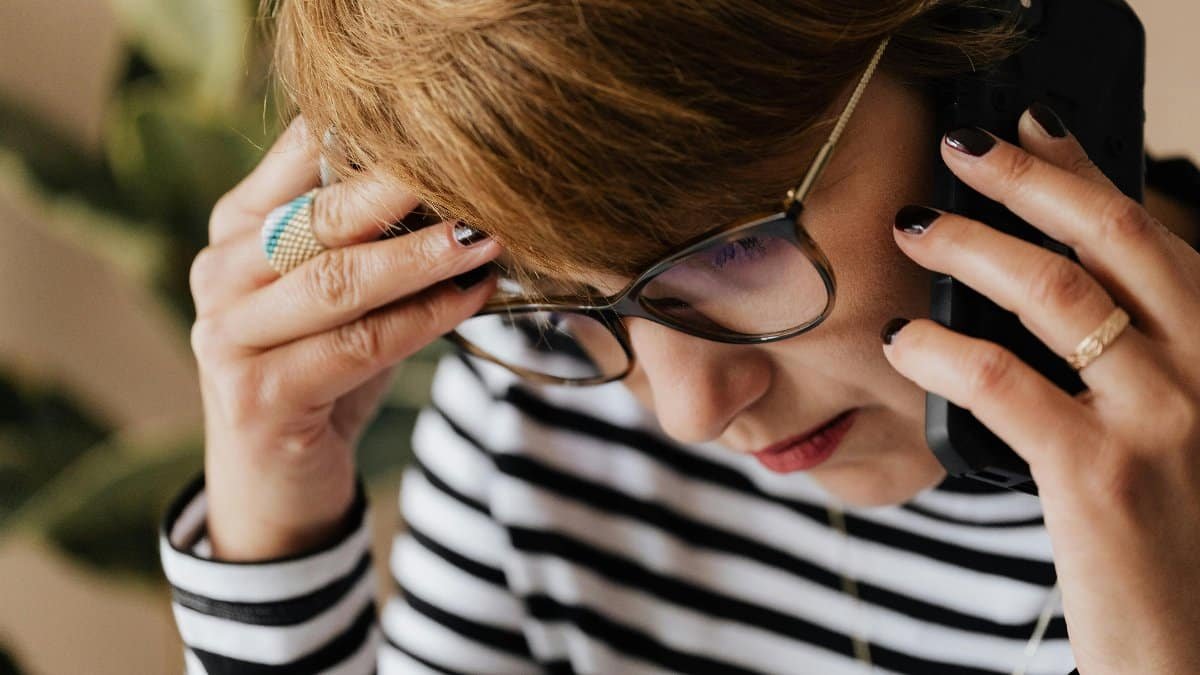 Focused woman with eyeglasses discussing work over a phone call, looking concerned and thoughtful. via Pexels