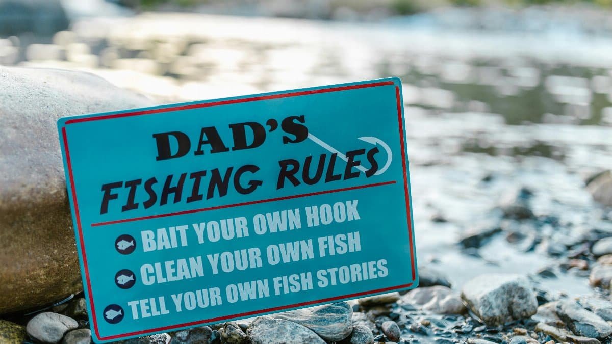 A close-up of a fun sign highlighting dad's fishing rules placed by a river, perfect for Father's Day. via Pexels