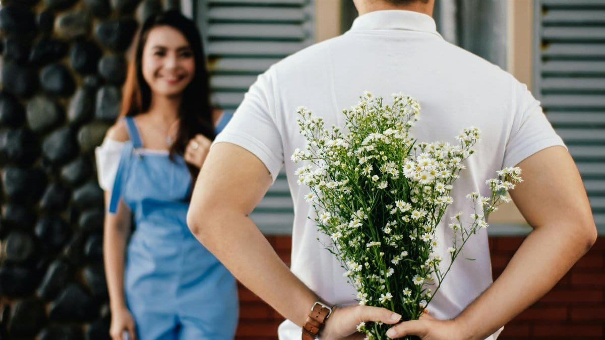 A man surprises his partner with flowers behind his back, symbolizing love and romance.
