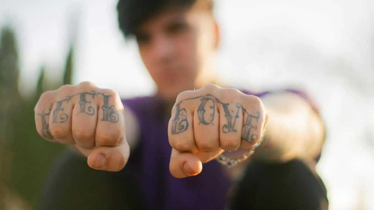Close-up of tattooed fists showing 'Love Hate' outdoors, emphasizing self-expression.