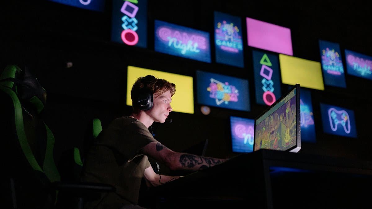 A focused gamer plays e-sports in a neon-lit room, surrounded by digital screens.