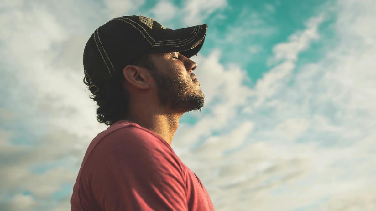 A man enjoys outdoor relaxation and mindfulness beneath a bright, cloudy sky, exuding calm and peace. via Pexels
