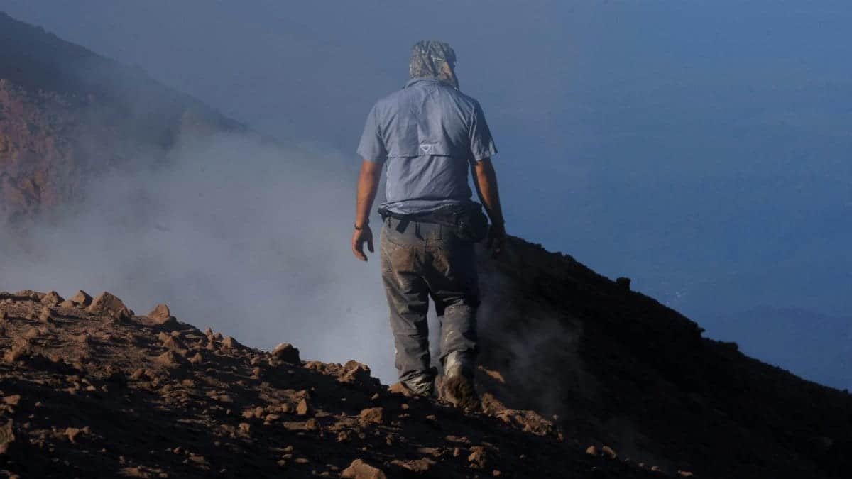 A solitary hiker in rugged terrain near volcanic smoke, showcasing adventure and resilience. via Pexels