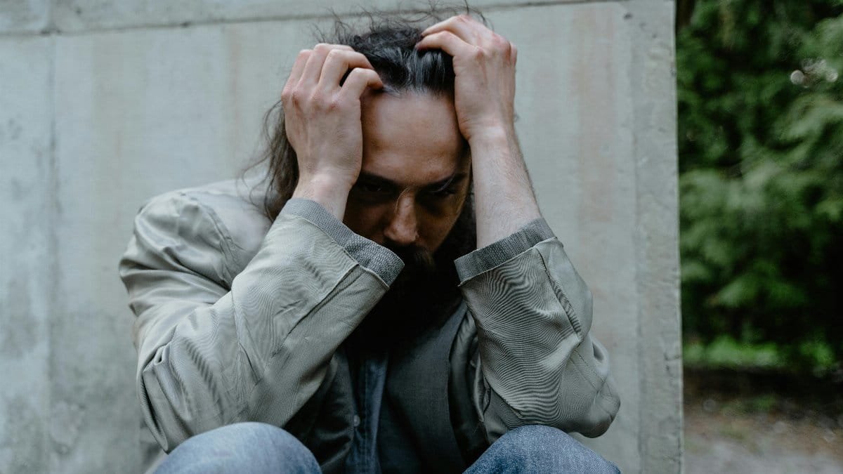 A pensive man sitting outdoors, expressing deep contemplation and emotional struggle.