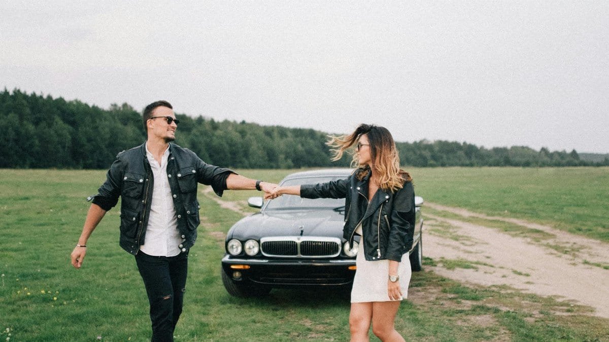 Happy couple in leather jackets holding hands near a black car outdoors. via Pexels