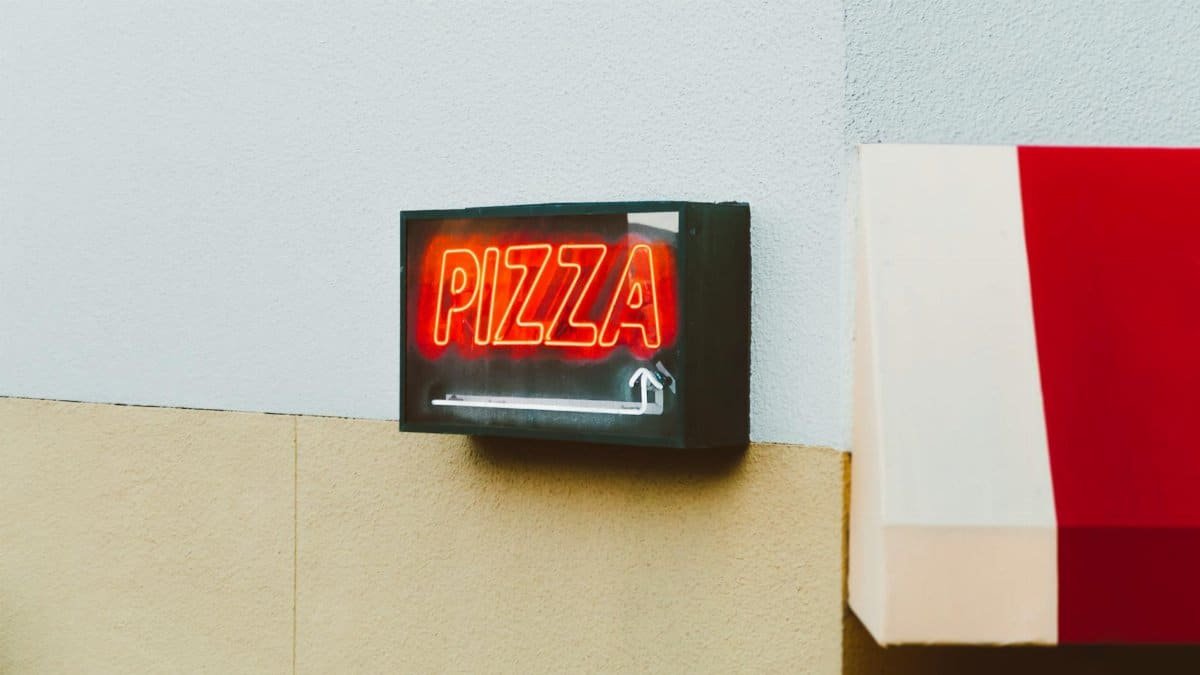 Bright neon pizza sign on the exterior of a San Francisco building, capturing vibrant urban life.