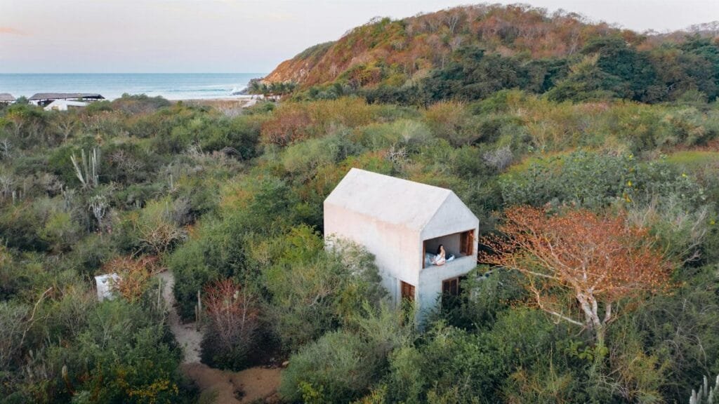 A serene modern house surrounded by dense foliage with ocean view, captured from above.