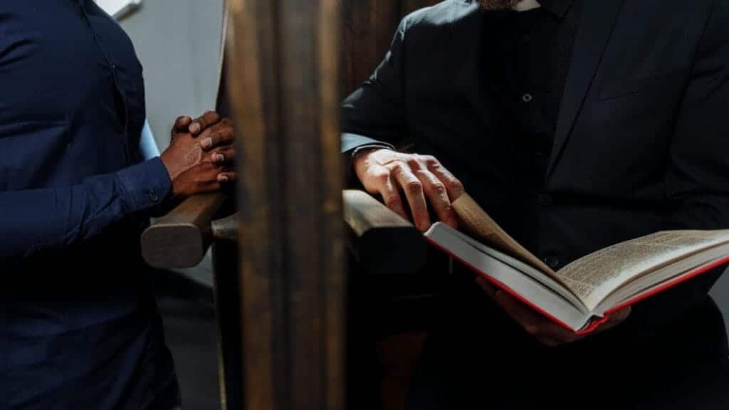 A priest listening to a man's confession inside a church, symbolizing faith and spirituality.