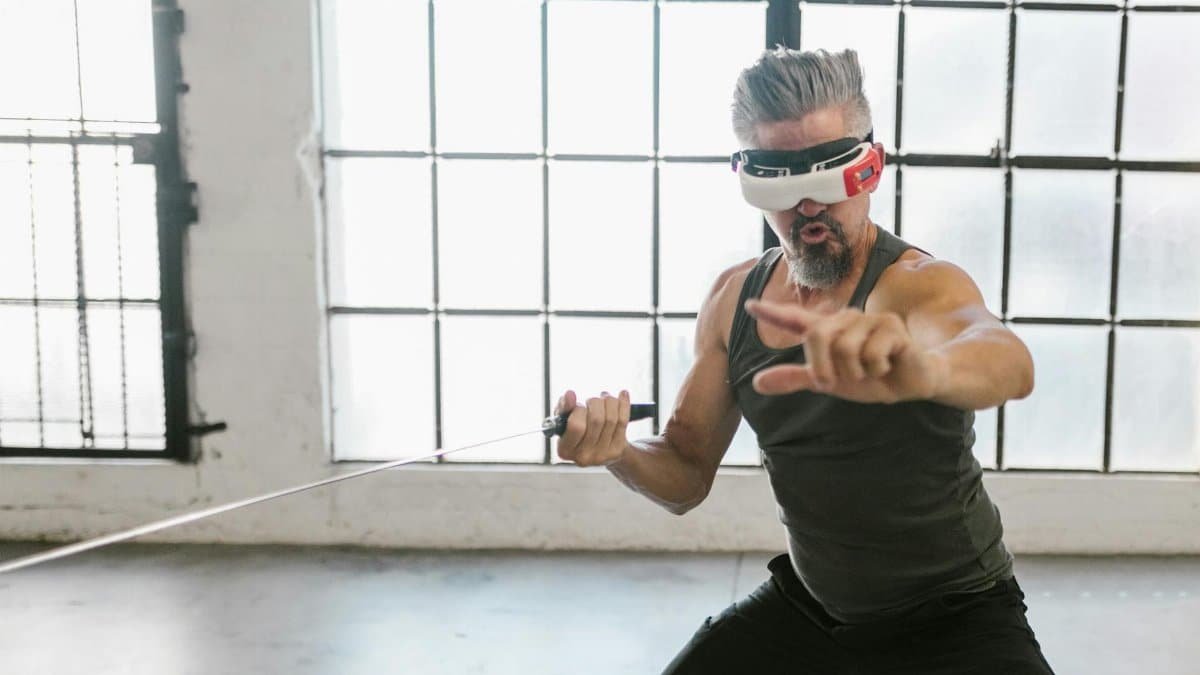 Adult man engaging in virtual training with a VR headset and sword indoors, showcasing future technology.