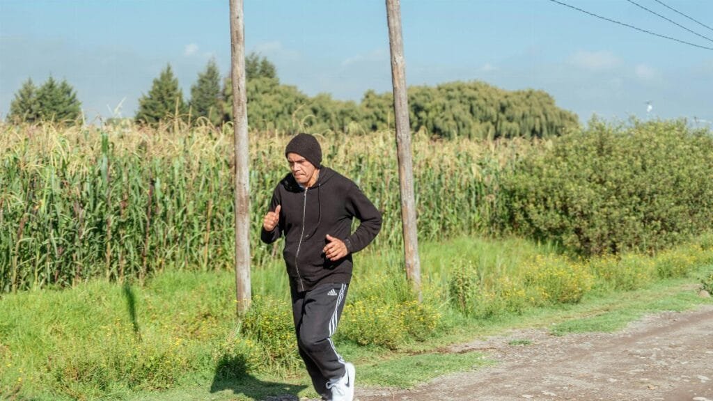 An adult man jogging on a rural dirt road beside a cornfield on a sunny day. via Pexels
