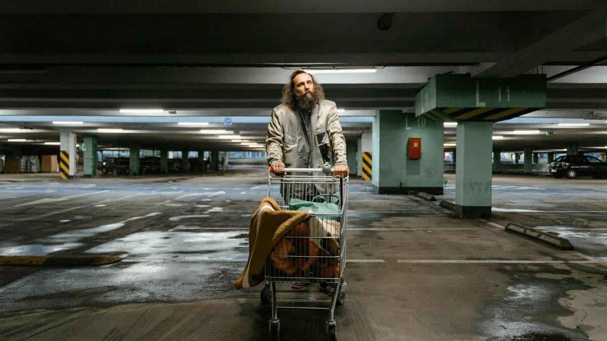 An elderly man with a shopping cart in an empty parking lot, symbolizing urban poverty.