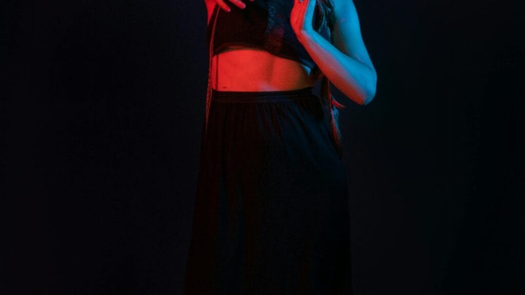 A female dancer poses gracefully under dramatic red and blue stage lighting. via Pexels