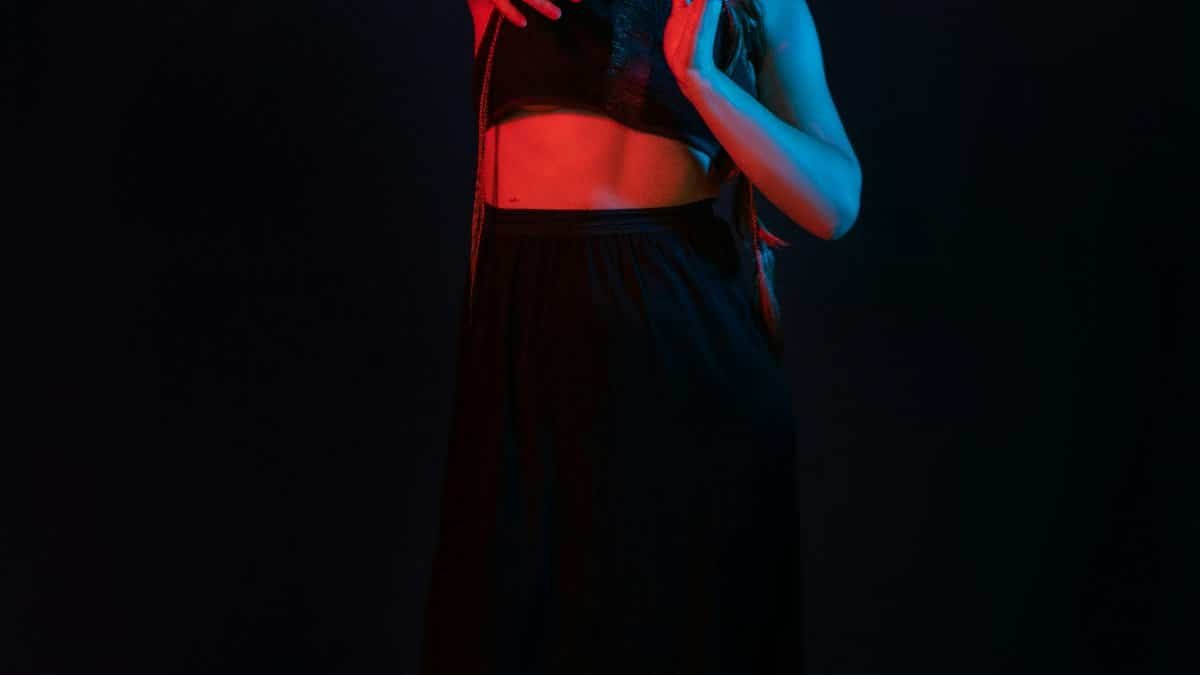 A female dancer poses gracefully under dramatic red and blue stage lighting. via Pexels