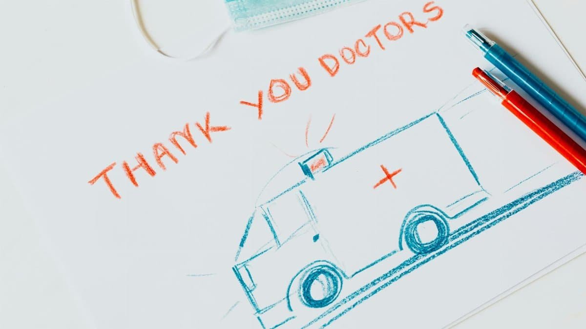 Handcrafted drawing of an ambulance expressing gratitude to doctors, accompanied by a face mask and colored pencils.