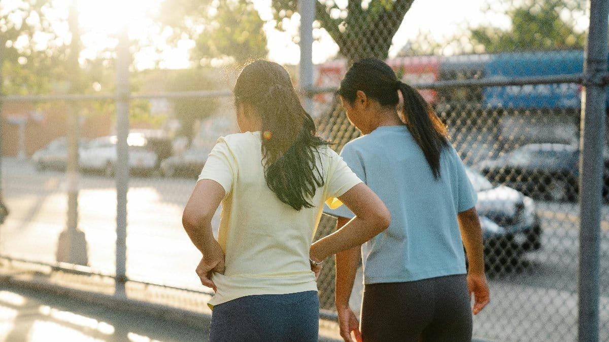 Back view of two women exercising near a chain-link fence on a sunny day.