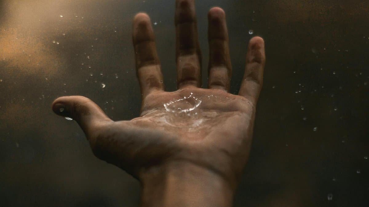 A close-up of an open hand catching raindrops against a dark background, showcasing water interaction.