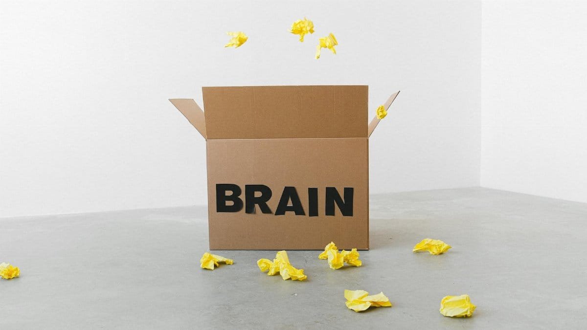 Crumpled yellow paper pieces on floor near carton box with Brain title on white background
