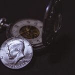 Close-up of a vintage silver coin with a pocket watch, symbolizing time and wealth.