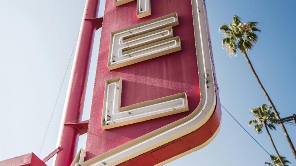 Vintage motel sign in Los Angeles with palm trees under a clear blue sky. via Pexels