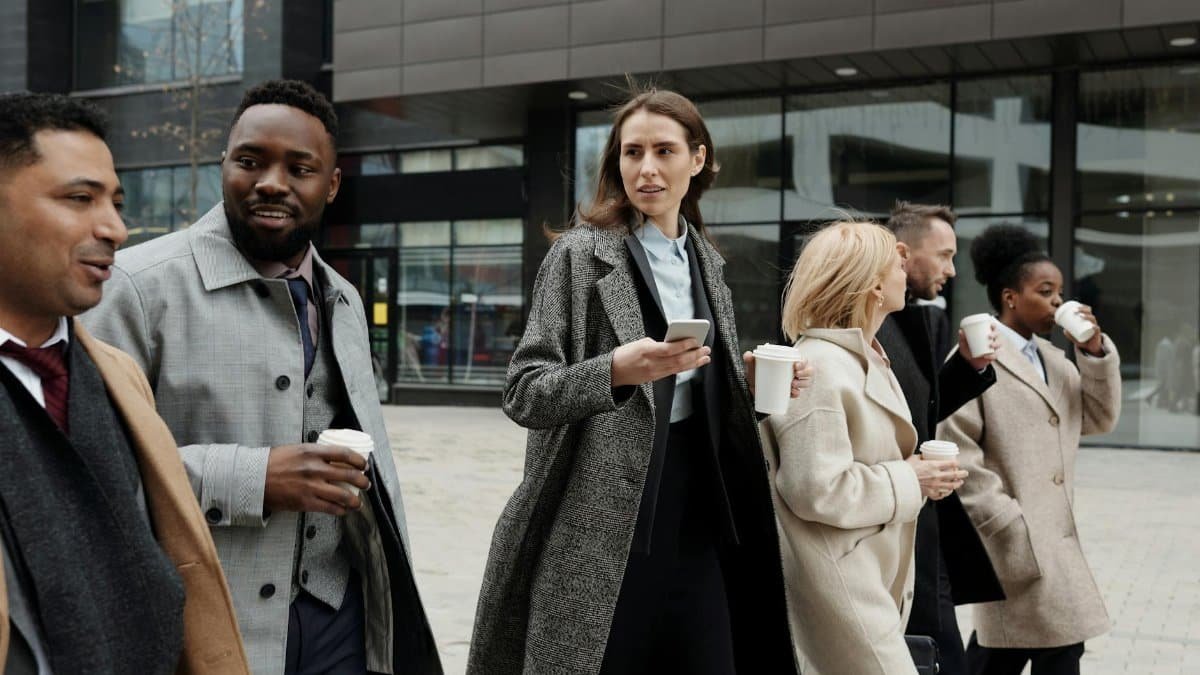 A diverse group of business professionals walking outside a modern building, enjoying coffee and conversation.