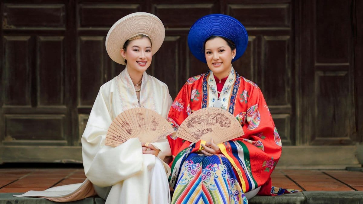 Two women in traditional Ao Dai attire, holding fans in Vietnam.