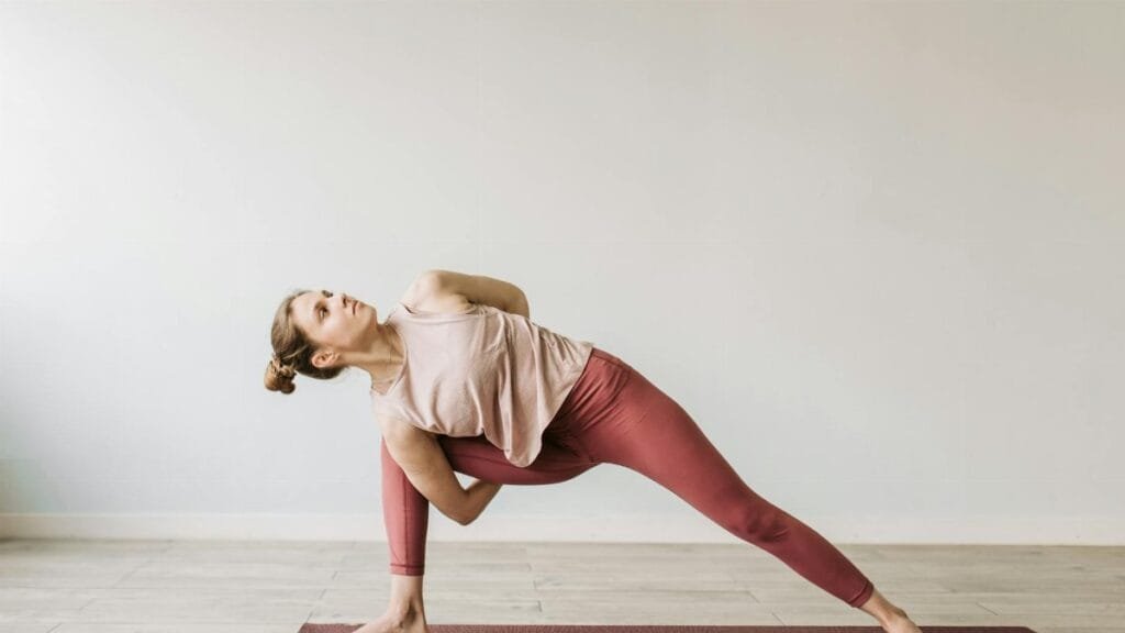 A woman practicing a yoga pose indoors on a mat, showcasing flexibility and wellness.