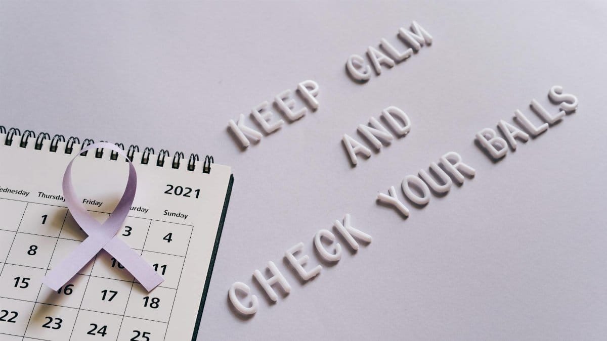 Flat lay image of a calendar with a purple ribbon and the text 'Keep Calm and Check Your Balls' for testicular cancer awareness.