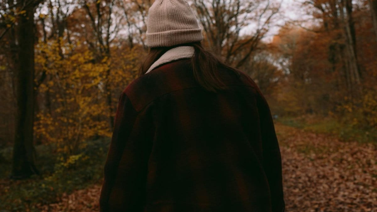A person walking through a fall forest wearing a cozy beanie and jacket, embracing nature.