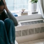 Frustrated young female having mental problem reflecting in mirror while sitting alone in room