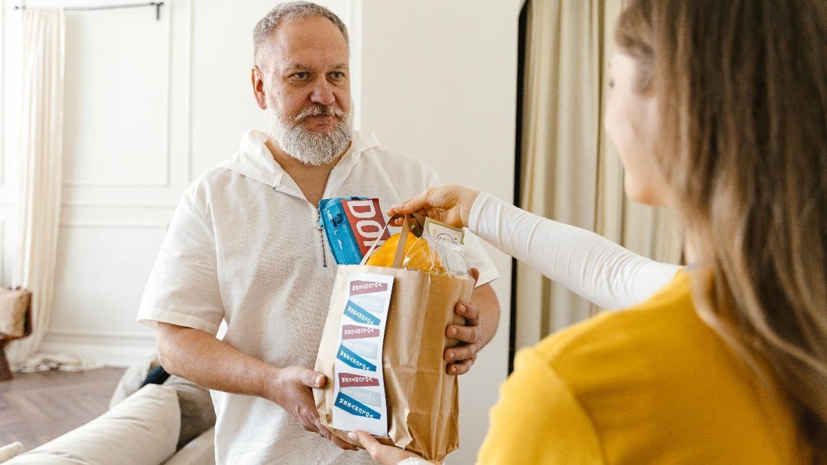 An elderly man with a beard receiving a donation in a paper bag indoors, highlighting community support.