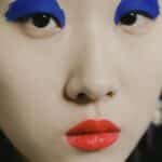 Striking close-up portrait of a person with bold blue eyeshadow and red lipstick.