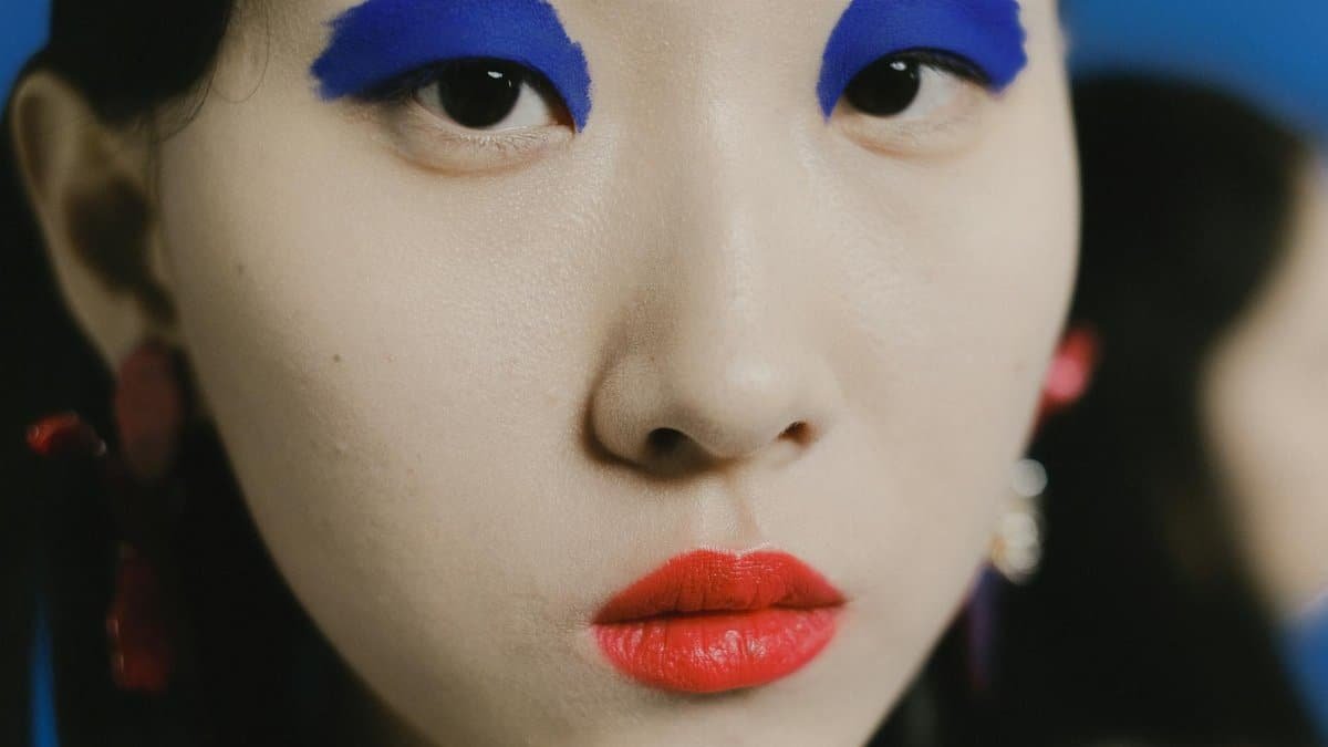 Striking close-up portrait of a person with bold blue eyeshadow and red lipstick.