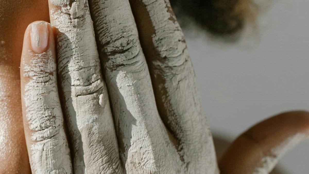 Close-up of a person with clay-covered hand on face, conveying creativity and expression.