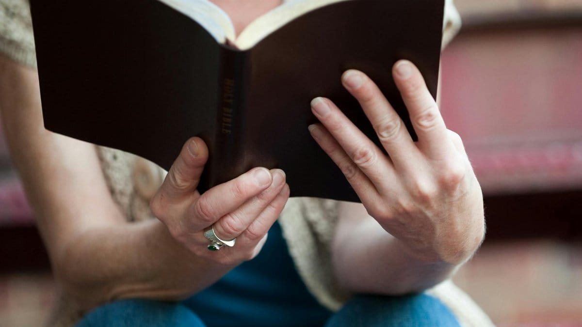 Hands holding an open Holy Bible, symbolizing faith and spirituality.