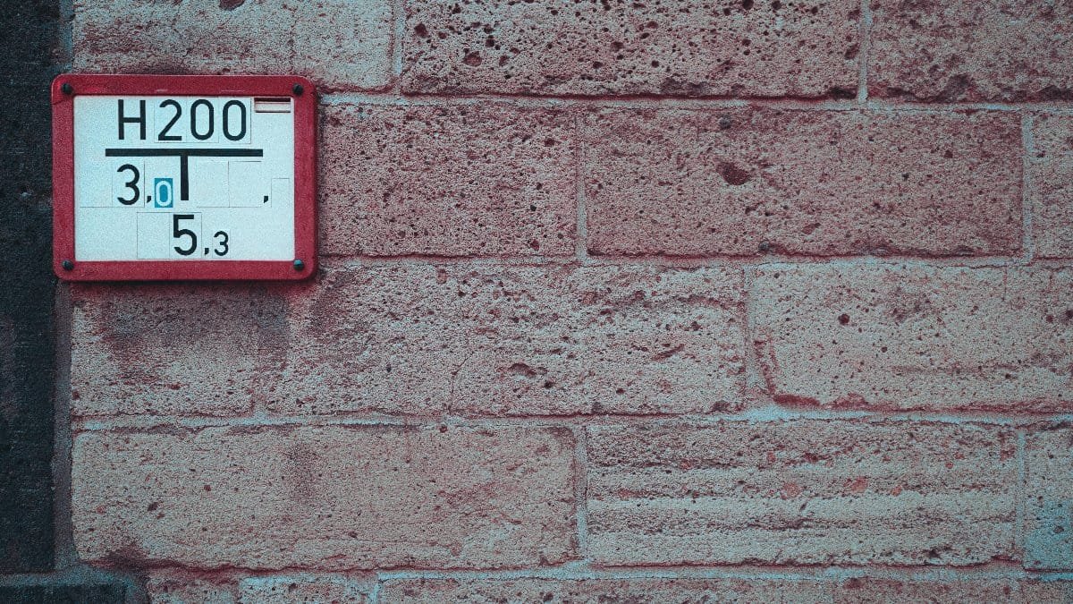 Close-up of a textured brick wall featuring a utility sign with numbers, offering urban detail.