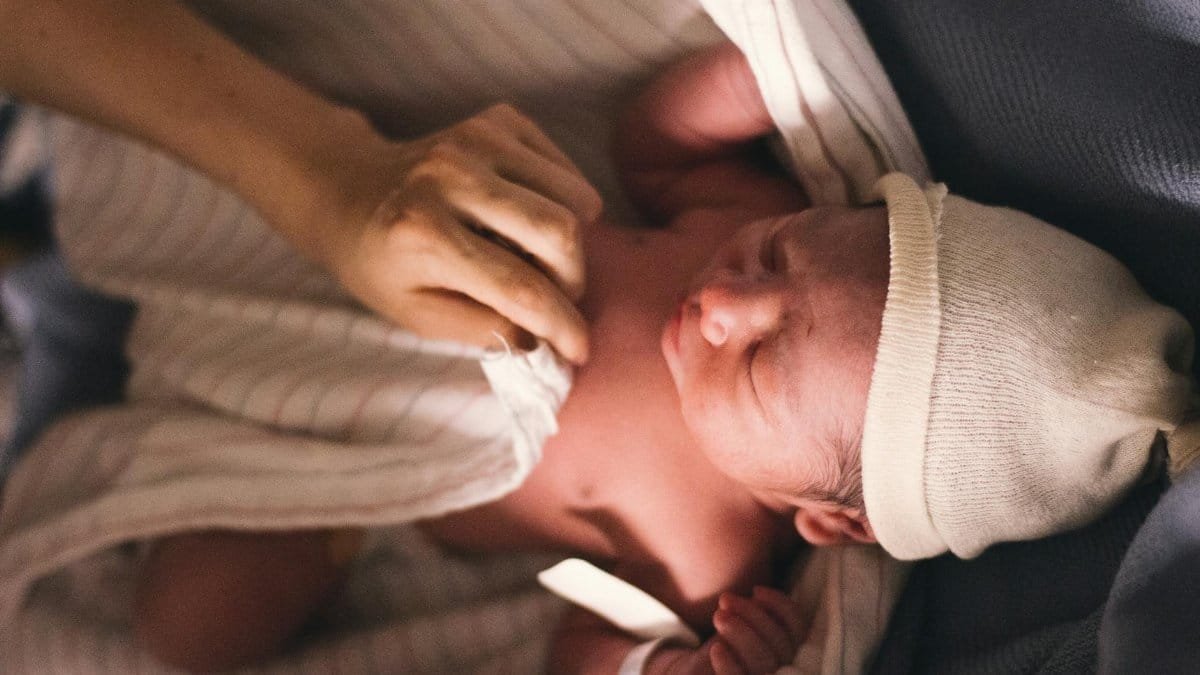 A serene moment of a newborn baby swaddled in blankets with a tender touch of a parent's hand.