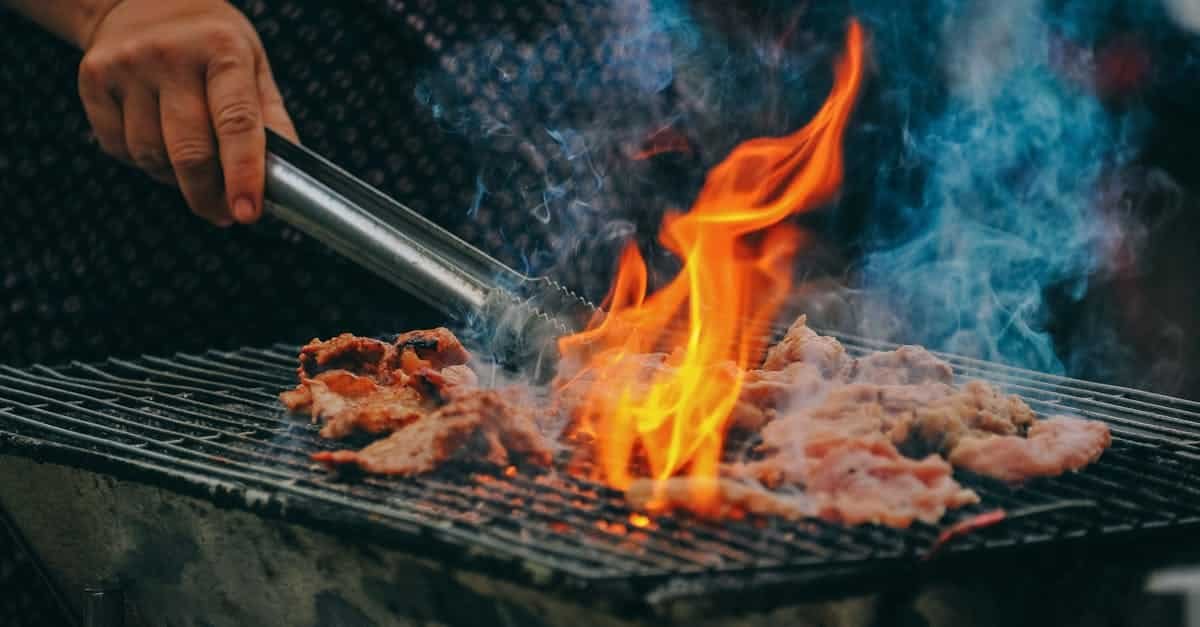Close-up of grilling meat with vibrant flames and smoky aura, showcasing outdoor cooking via Pexels
