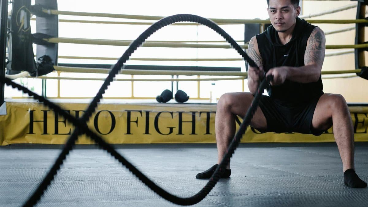 A muscular man performing an intense battle rope workout in a gym setting, showcasing strength and endurance.