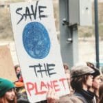 A climate change protest in Prague, with people holding environmental signs like 'Save the Planet'.