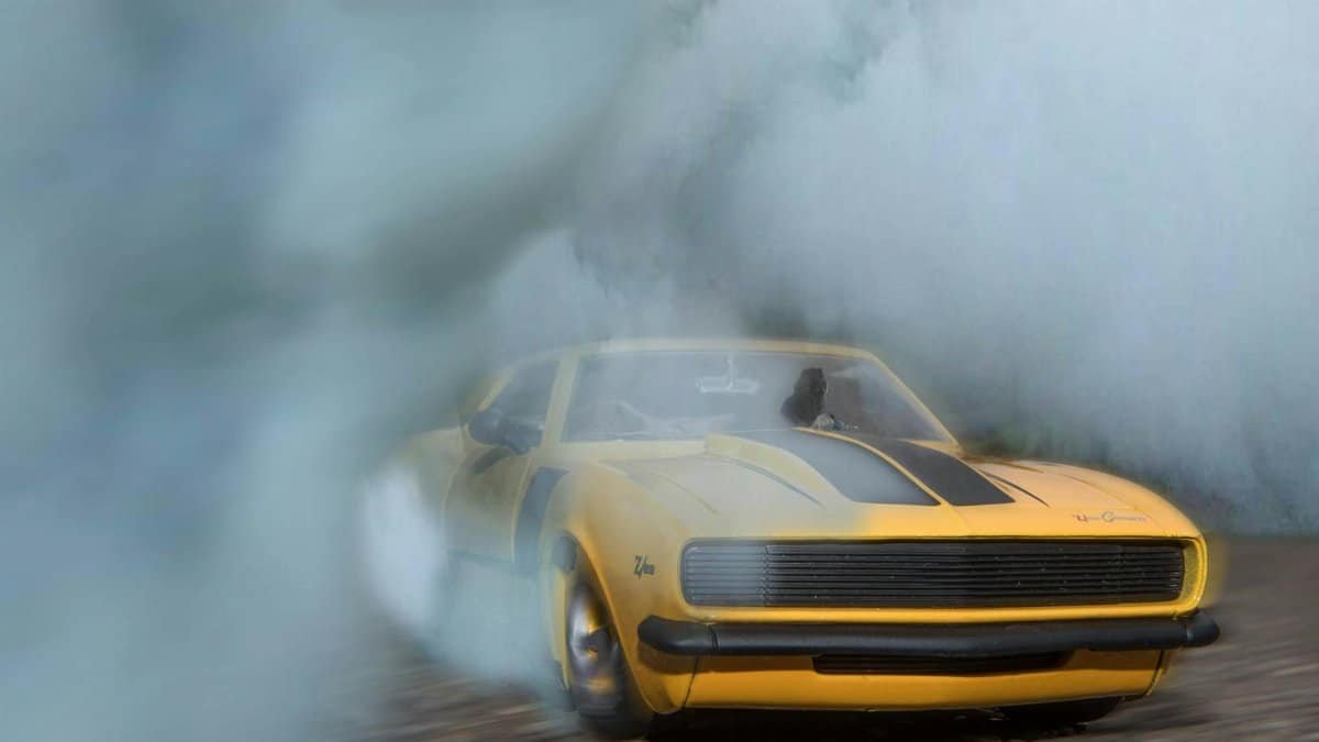 1969 Camaro drifting on pavement with smoke engulfing the car, showcasing its power.