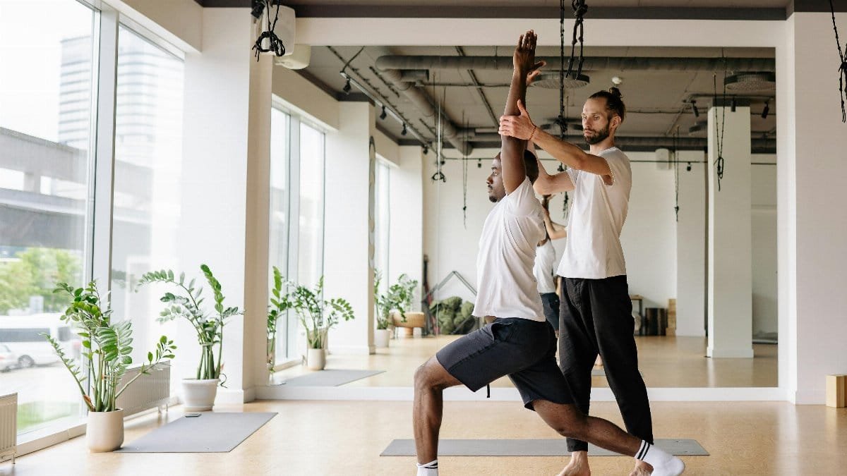 Instructor guides student in yoga pose in bright, modern studio. via Pexels