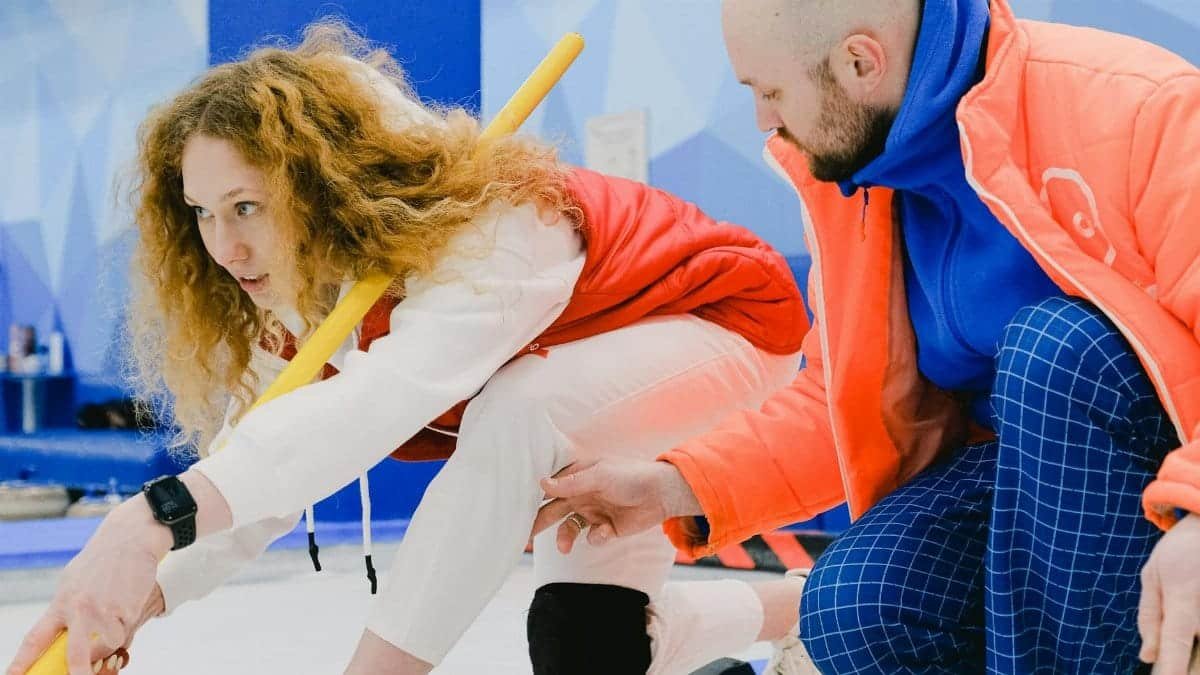 Two adults engaged in curling practice indoors, depicting focus and teamwork.