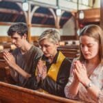 Adults praying together in a serene church interior, fostering religious devotion. via Pexels
