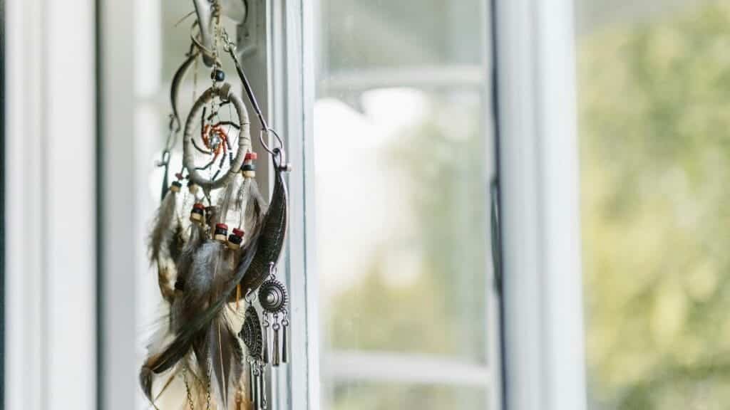 A dreamcatcher with feathers hangs by a sunlit window, creating a serene ambiance.