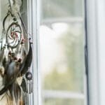 A dreamcatcher with feathers hangs by a sunlit window, creating a serene ambiance.
