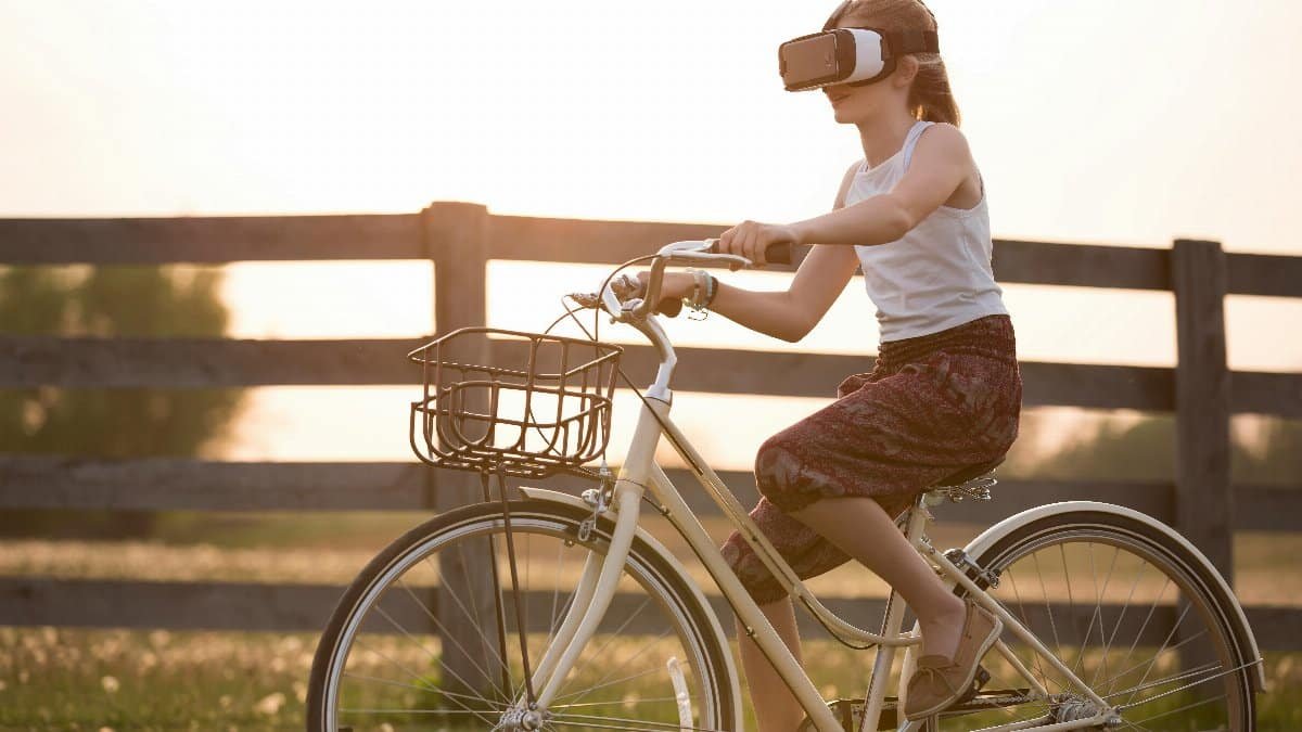 A teenager enjoys virtual reality while riding a bicycle outdoors at sunset.