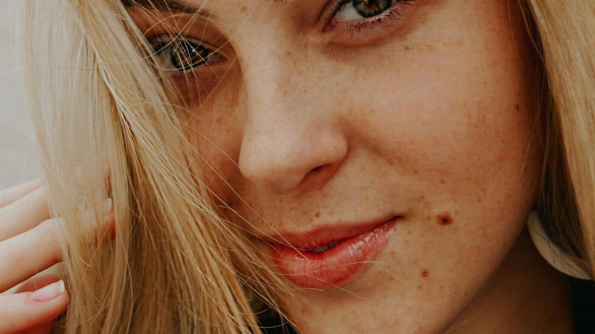Charming close-up portrait of a smiling blonde woman with natural makeup and freckles.