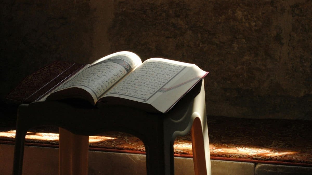 A Quran rests on a stool inside a mosque with sunlight casting dramatic shadows. via Pexels
