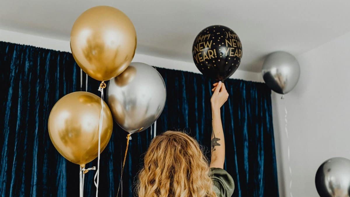 Woman preparing for a New Year party with gold and silver balloons indoors.