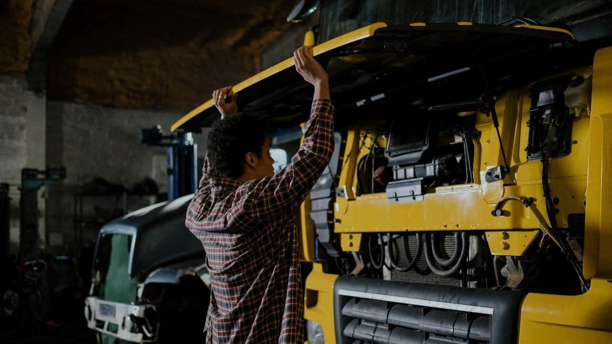 A mechanic inspecting a truck engine in a garage setting, wearing plaid shirt.